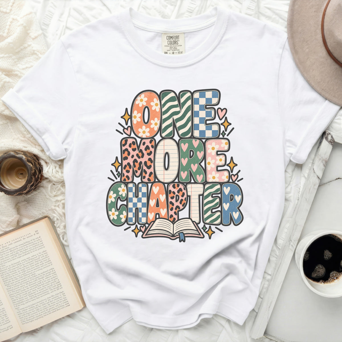 White t-shirt with "ONE MORE CHAPTER" graphic and open book.