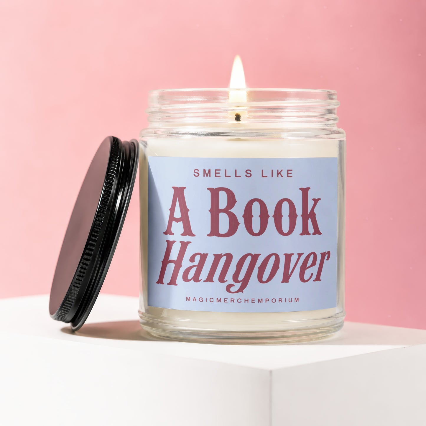 Lit candle in a jar with a black lid, reading "Smells Like A Book Hangover".