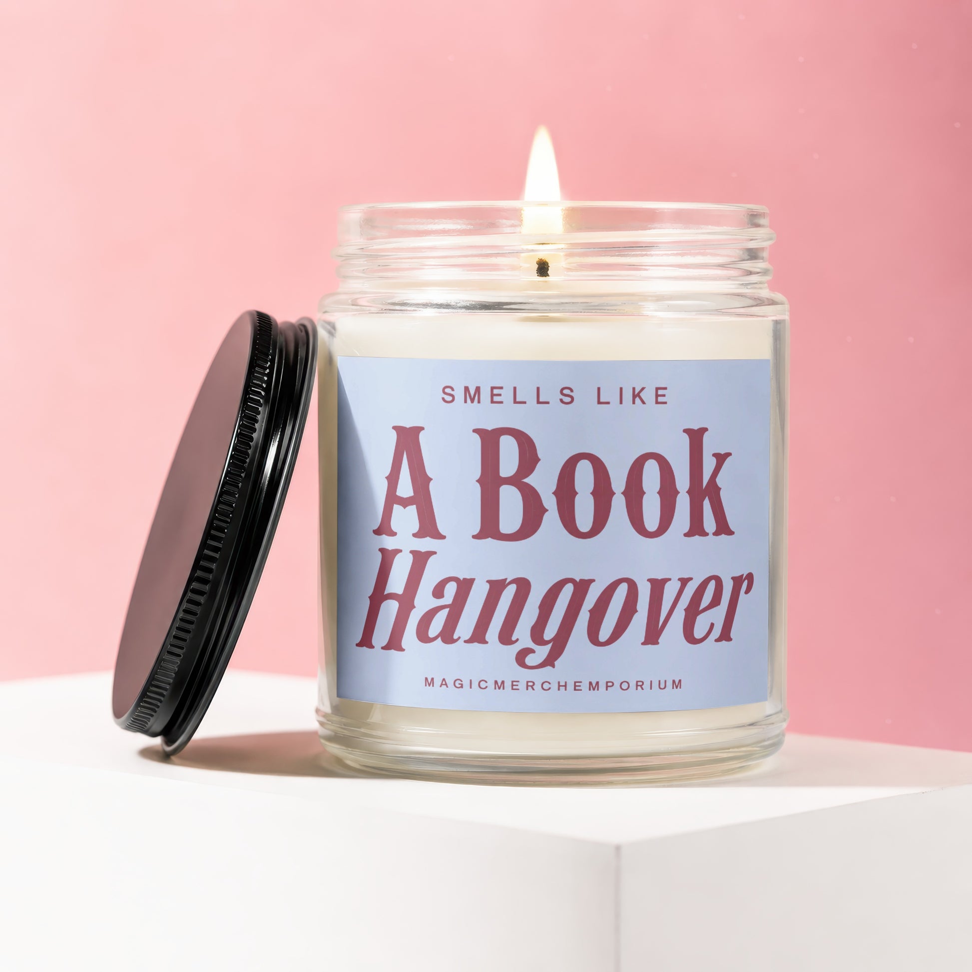 Lit candle in a jar with a black lid, reading "Smells Like A Book Hangover".