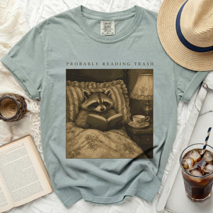 T-shirt with graphic of raccoon reading in bed, "PROBABLY READING TRASH" text.