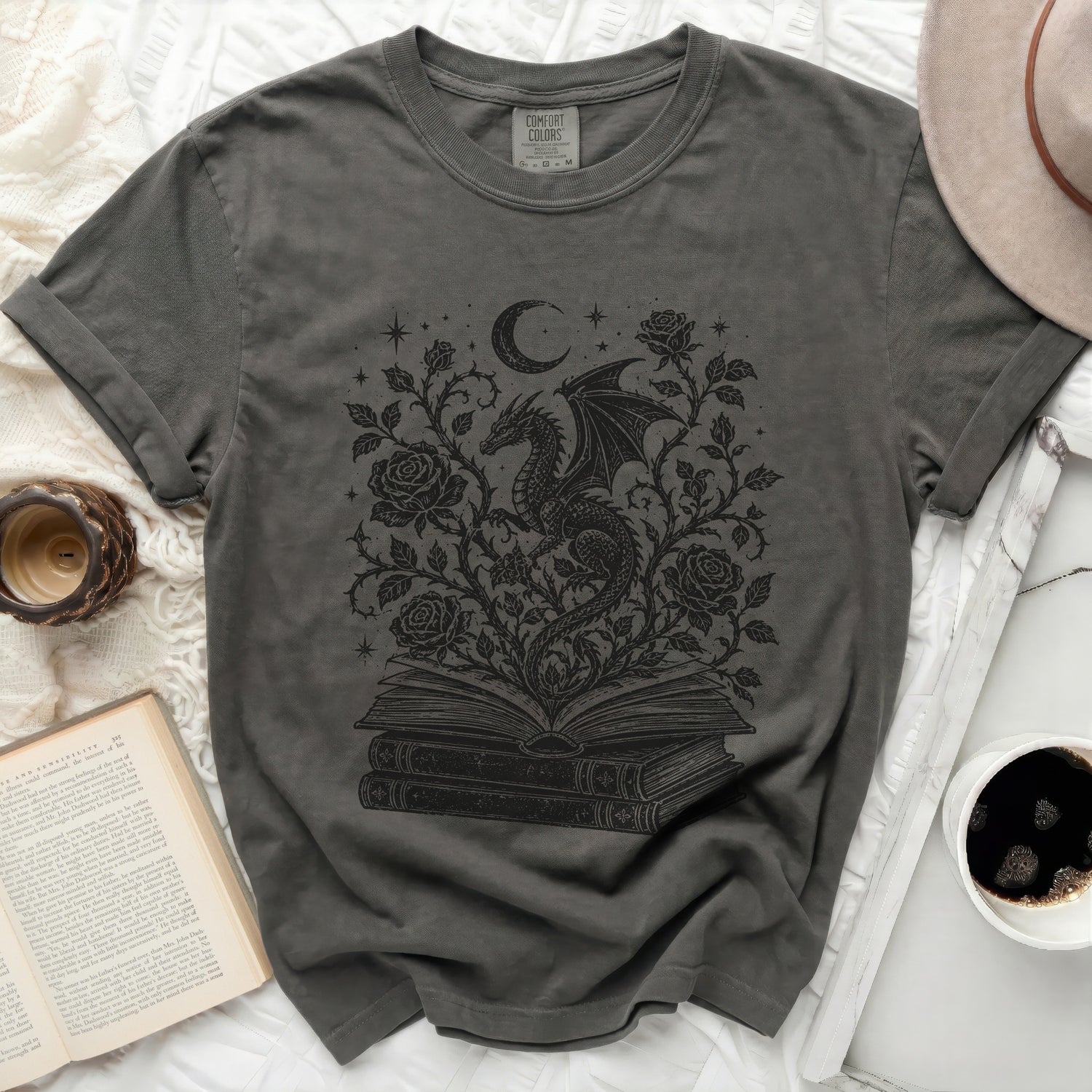 Grey t-shirt with a black dragon moon and roses graphic on an open book.