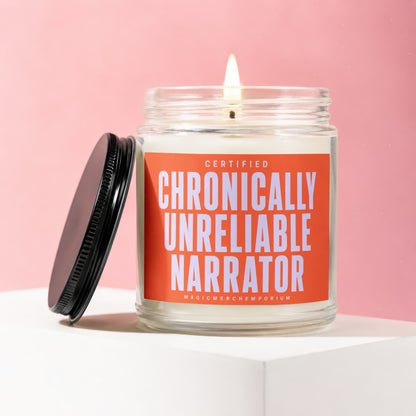 Glass jar candle with lit flame, black lid, and orange label reading "CERTIFIED CHRONICALLY UNRELIABLE NARRATOR".