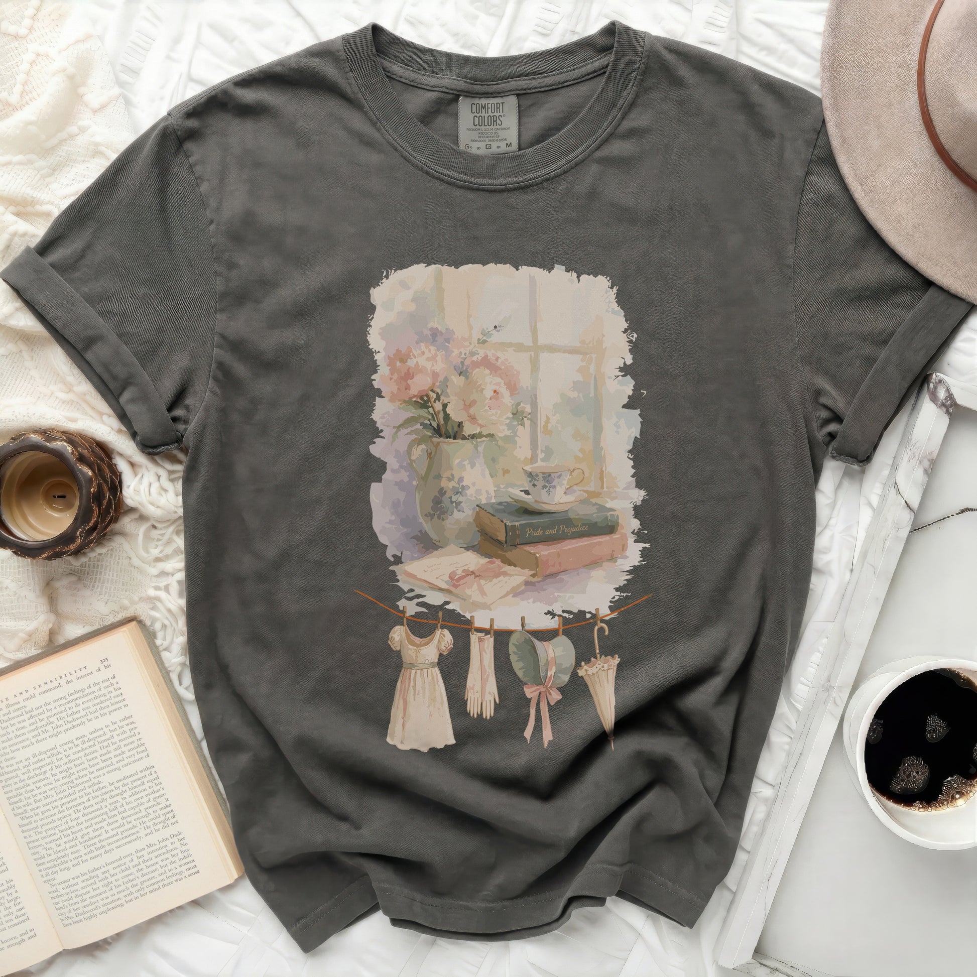 T-shirt with watercolor print of flowers, books, and vintage clothing on clothesline.