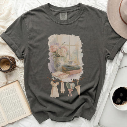 T-shirt with watercolor print of flowers, books, and vintage clothing on clothesline.