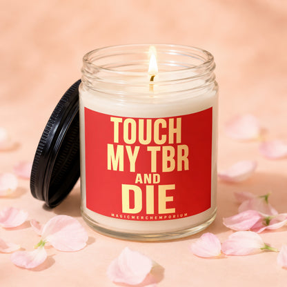 Glass candle with lit wick and red label reading "TOUCH MY TBR AND DIE".