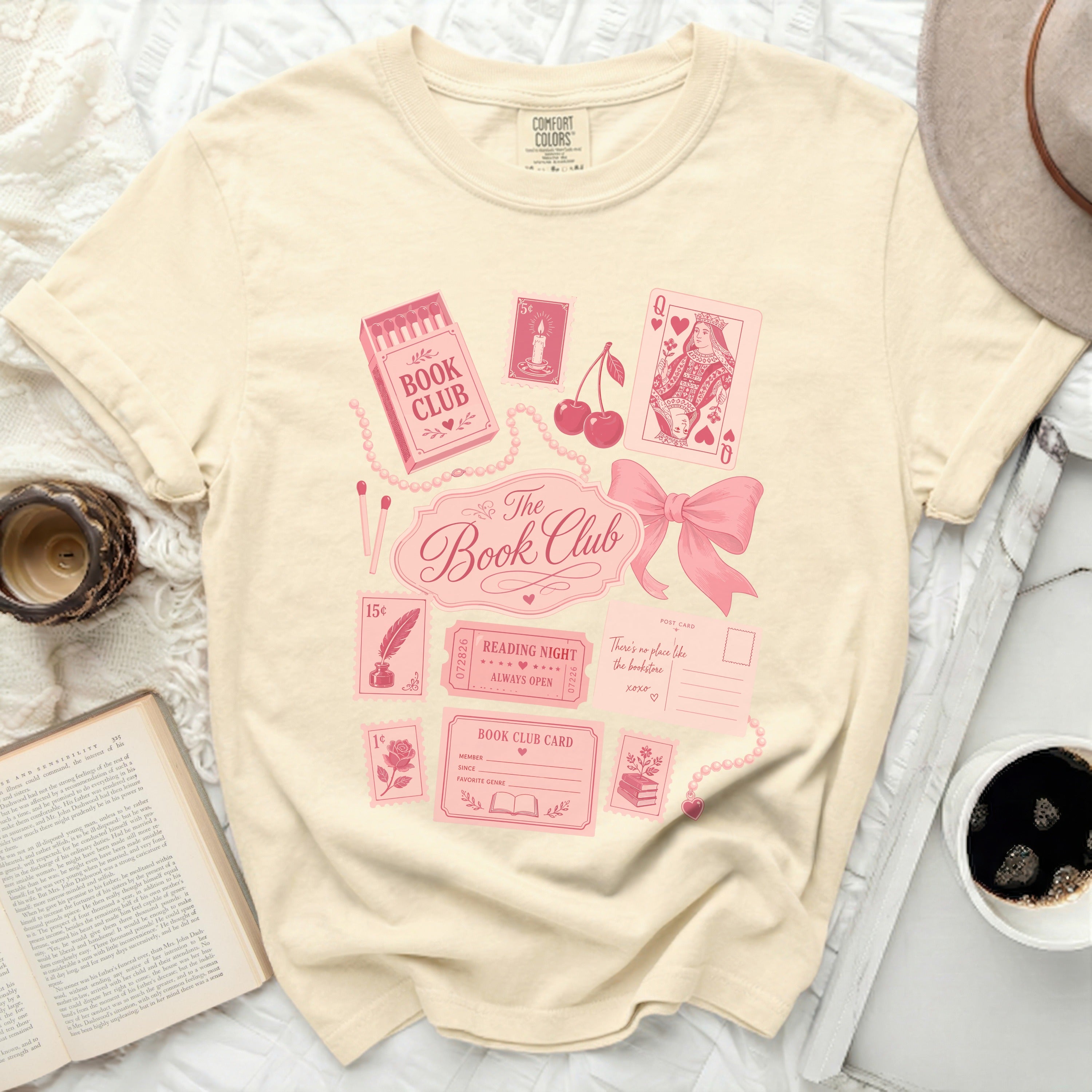 Cream t-shirt with pink book club graphics, playing cards, and postage stamps.