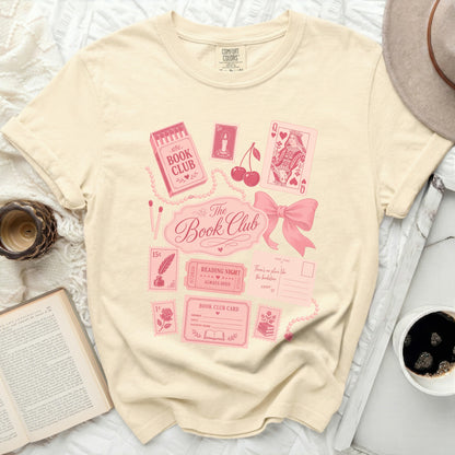 Cream t-shirt with pink book club graphics, playing cards, and postage stamps.