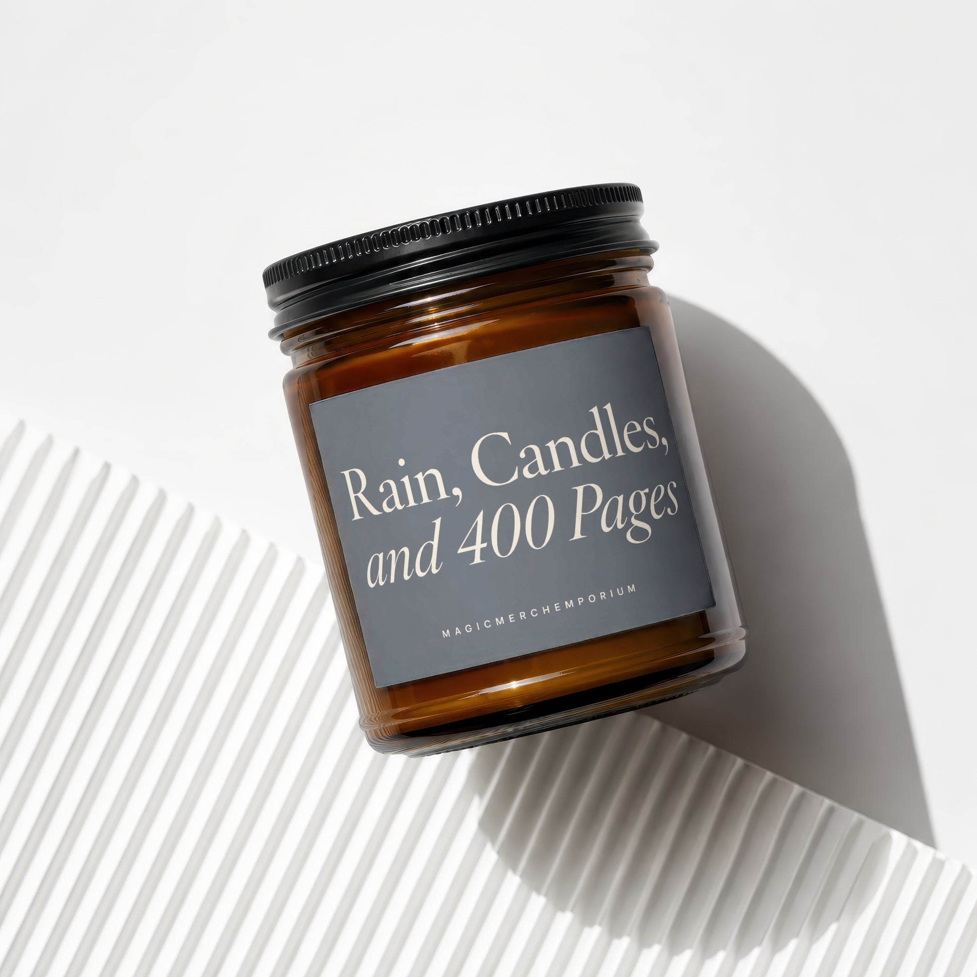 Amber glass candle with black lid inscribed "Rain, Candles, and 400 Pages".