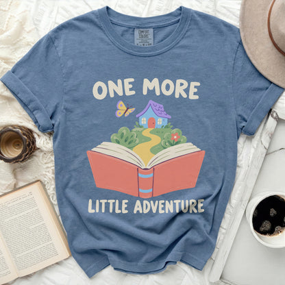 Blue t-shirt with illustration of open book, house, and butterfly; text "ONE MORE LITTLE ADVENTURE".