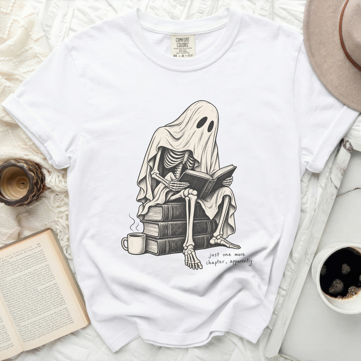 Skeleton in ghost costume reading a book with text "just one more chapter, apparently."