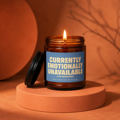 Lit amber jar candle with blue label reading "Currently Emotionally Unavailable (I'm Reading)".