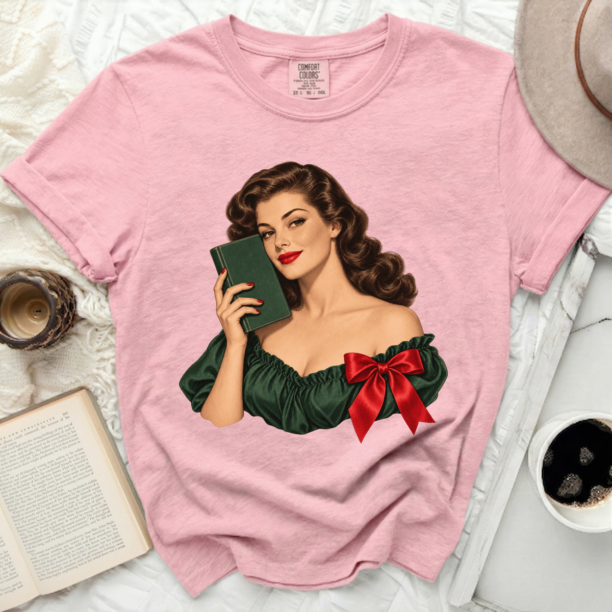 Pink t-shirt with graphic of woman in green dress holding a book.