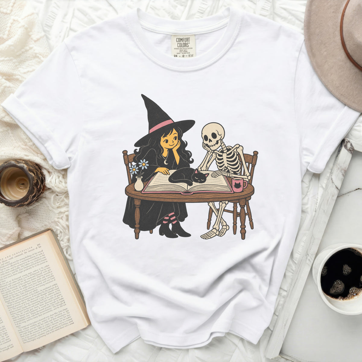 White t-shirt with witch, skeleton, cat, and book graphic; Comfort Colors label.