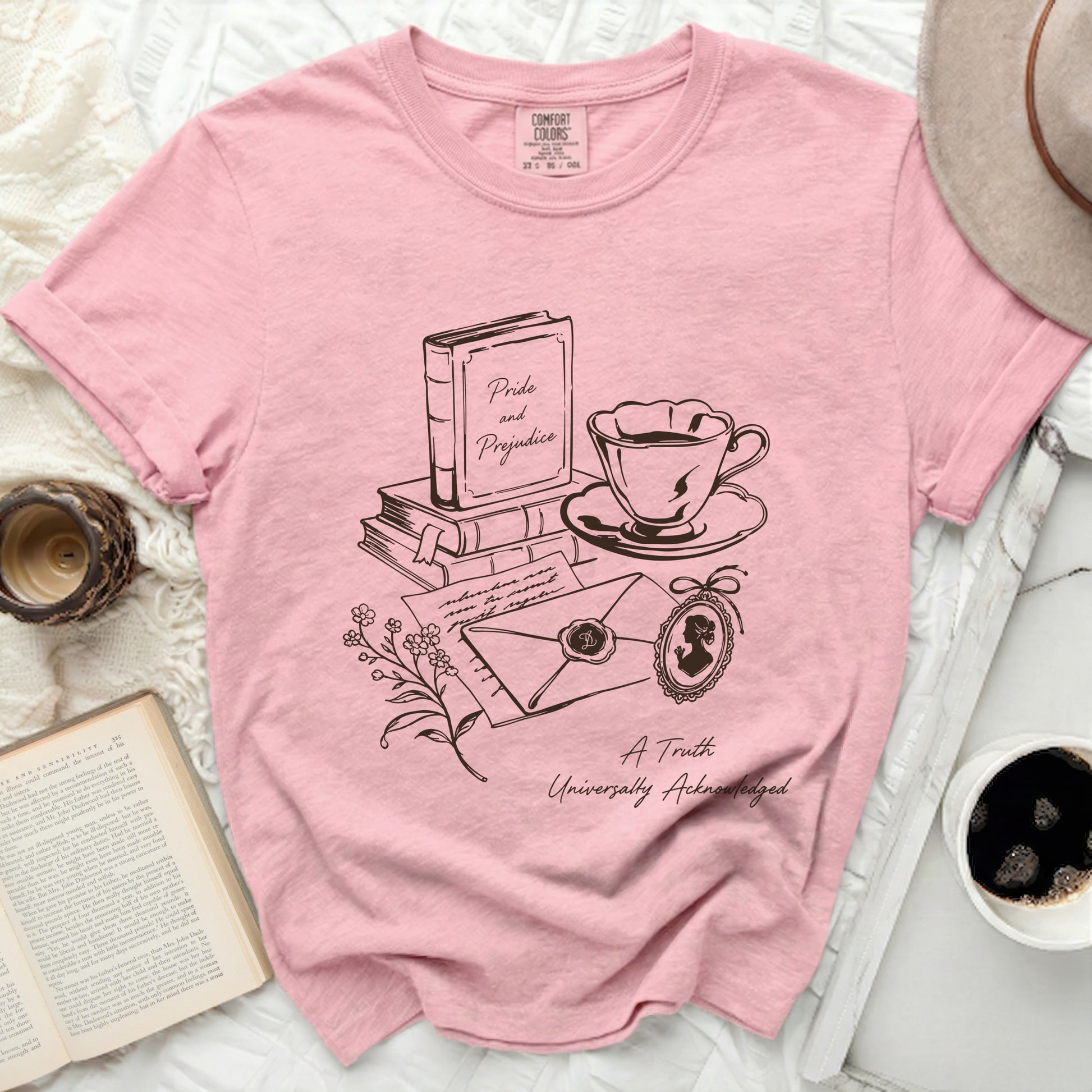 Pink shirt with line art of "Pride and Prejudice" book, teacup, envelope, and cameo.