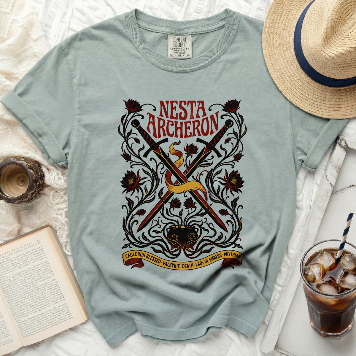 Green t-shirt with "Nesta Archeron" design, swords, cauldron, and floral elements.
