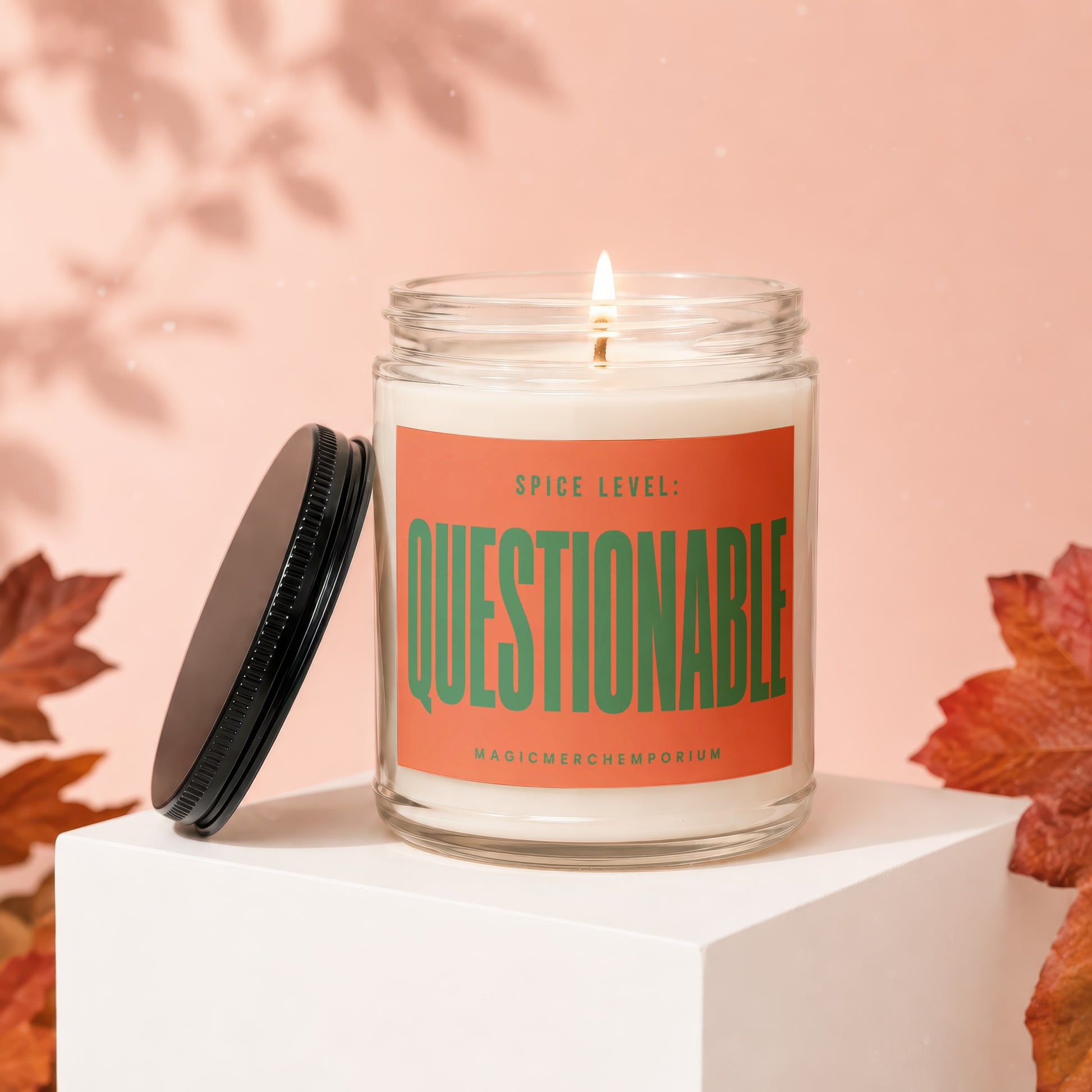 Jar candle with orange label reading "SPICE LEVEL: QUESTIONABLE" and "MAGICMERCH..."