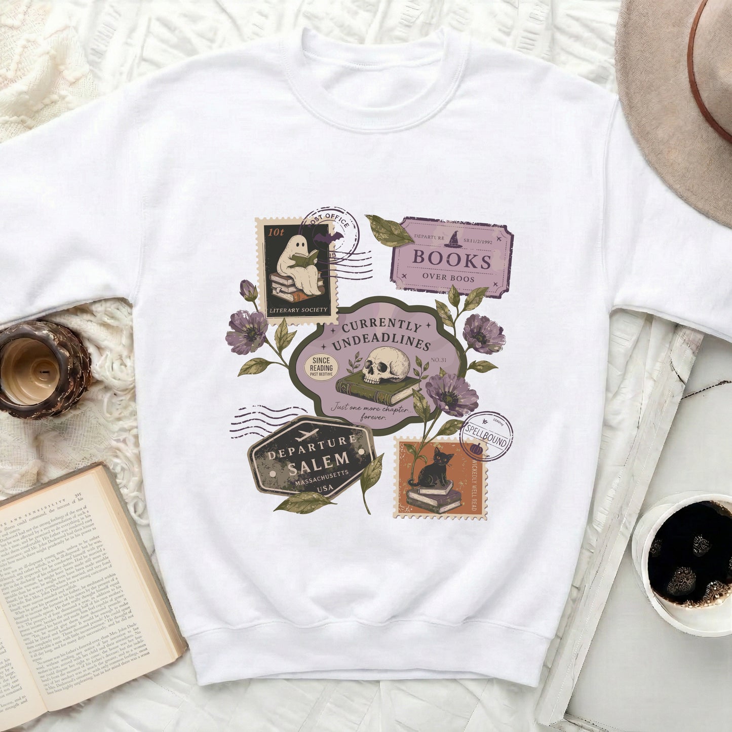 White sweatshirt with graphic featuring ghost, skull, cat, books, and stamps.