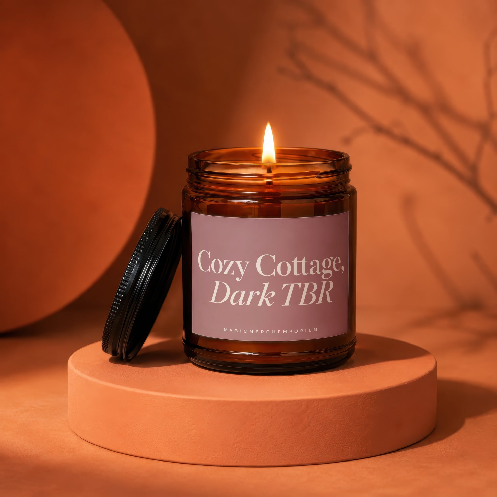 Amber jar candle labeled "Cozy Cottage, Dark TBR" on an orange pedestal.