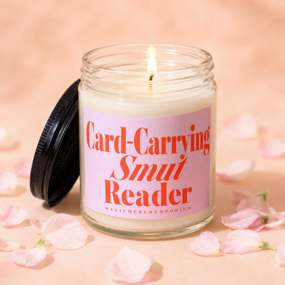 Burning candle with pink label reading "Card-Carrying Smut Reader".