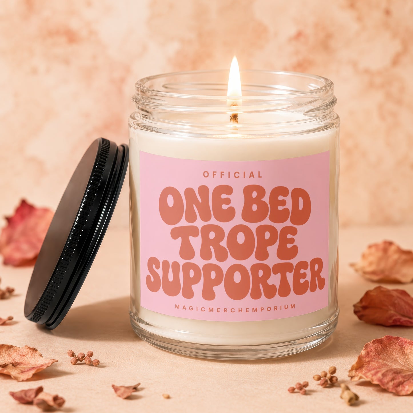 Candle with pink label reading "OFFICIAL ONE BED TROPE SUPPORTER"