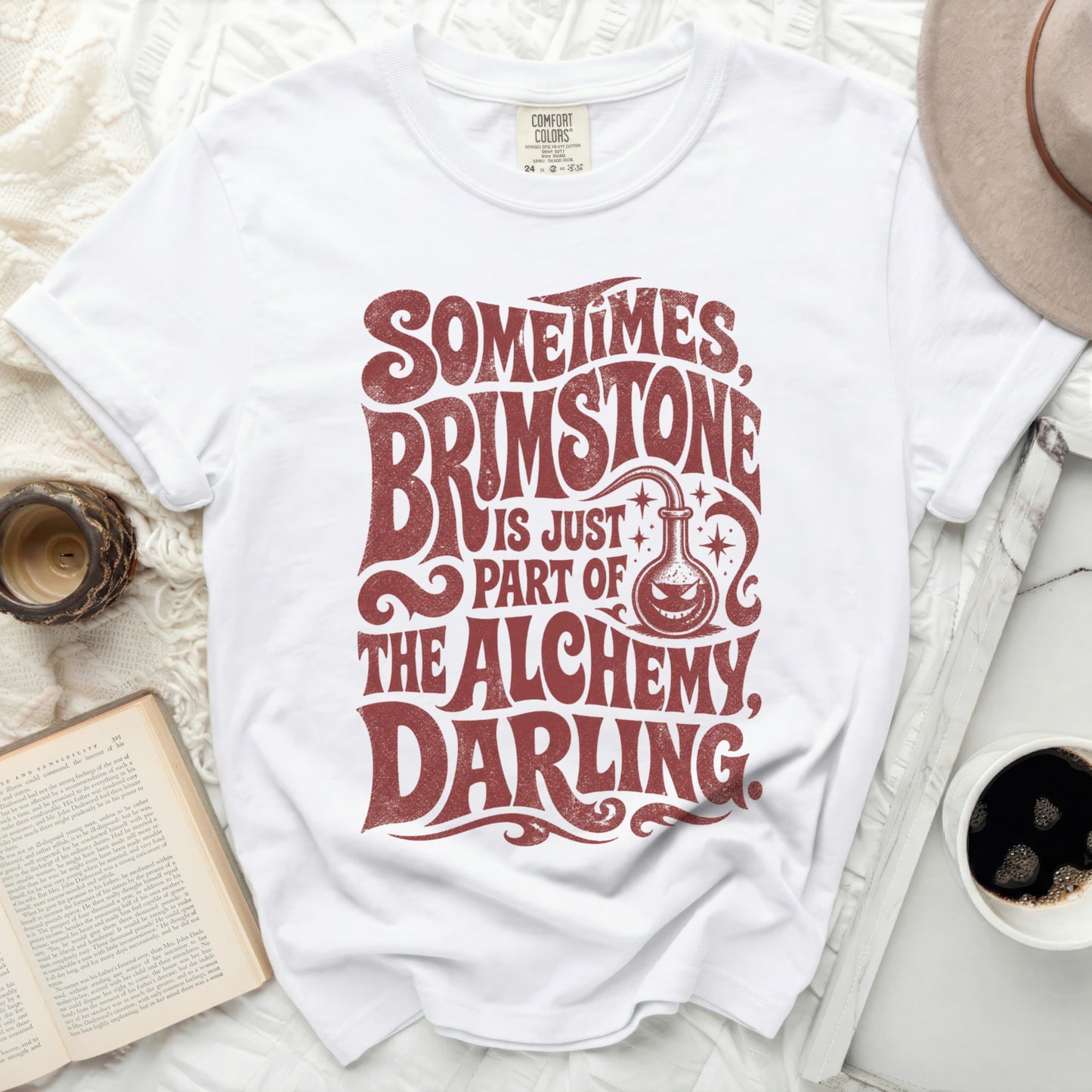 White t-shirt with "Sometimes Brimstone Is Just Part Of The Alchemy, Darling" text.