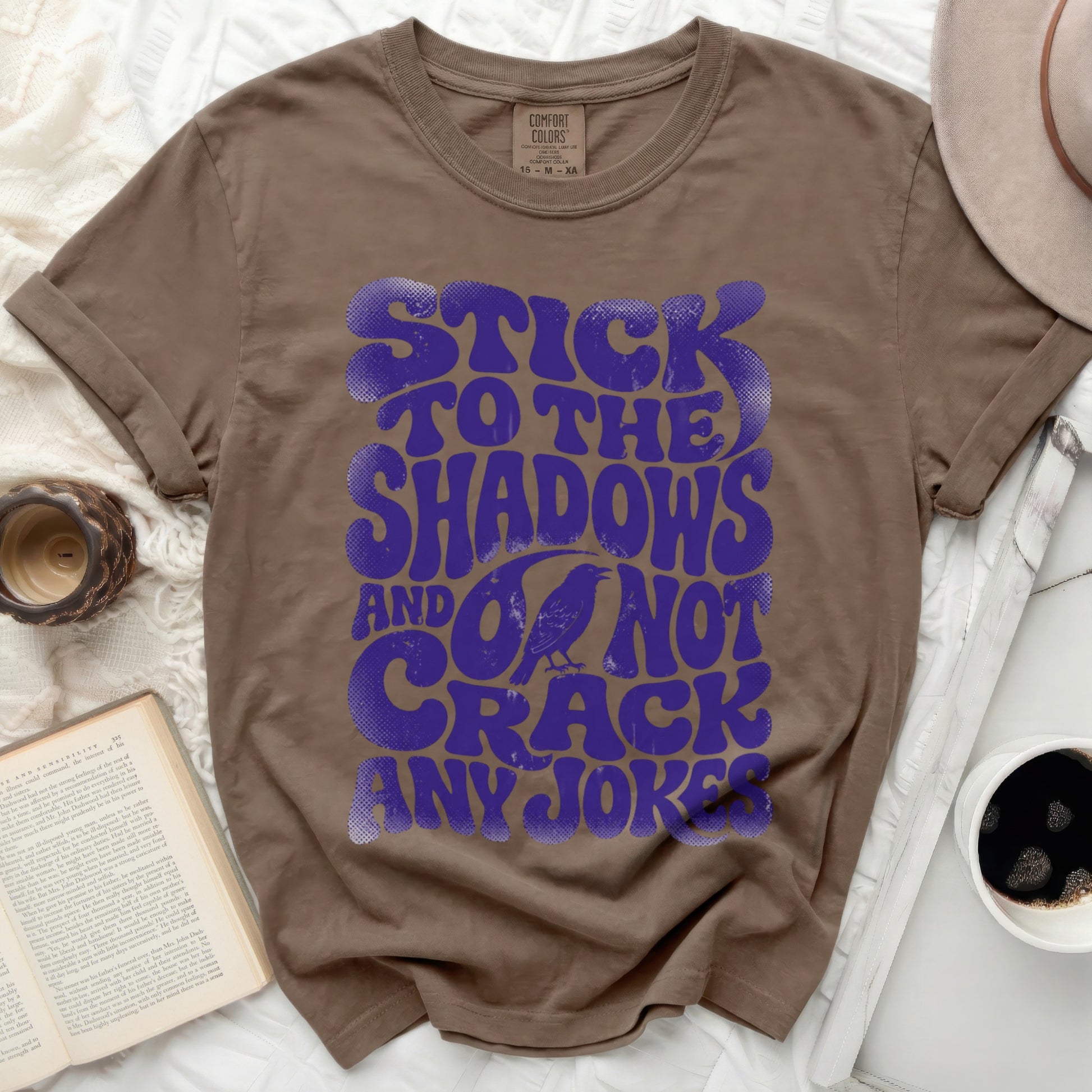 Brown t-shirt with purple text "Stick to the shadows and do not crack any joker" and a crow.