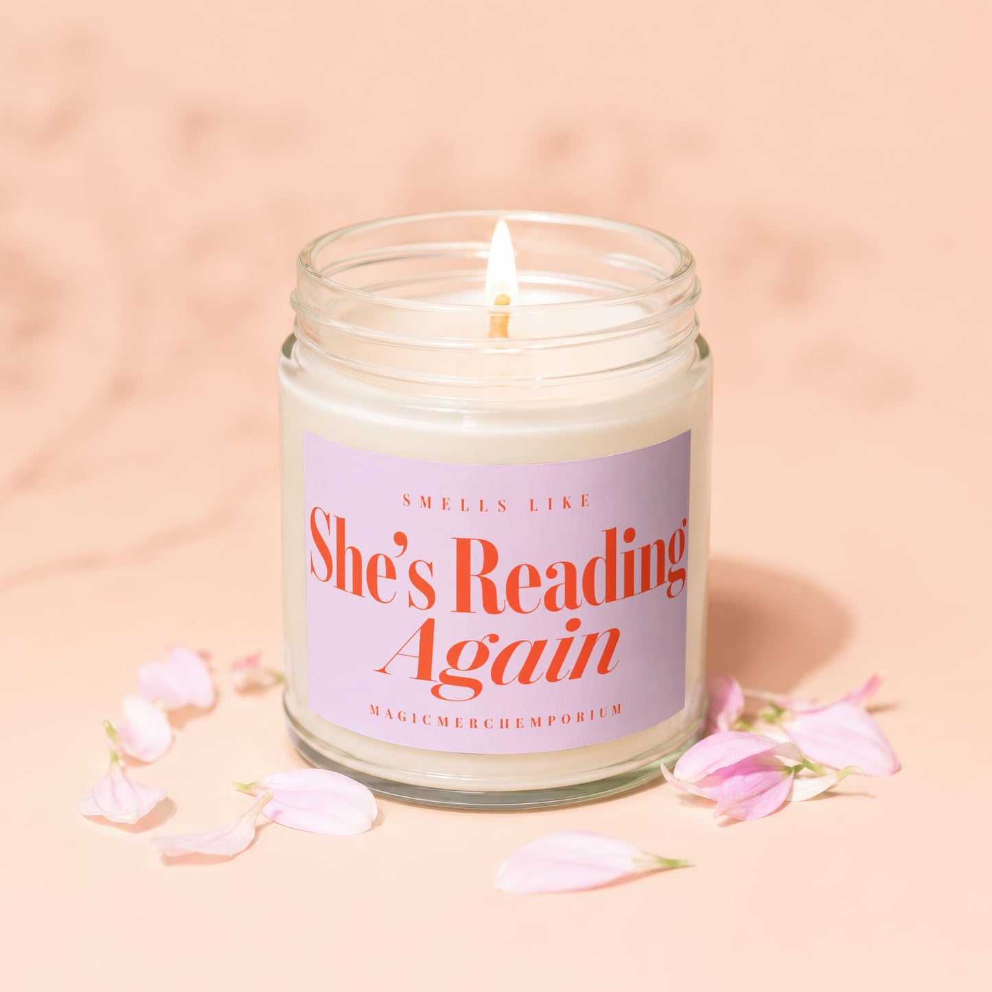 Candle with lit wick, reads "Smells like She's Reading Again. Magicmerch.emporium".
