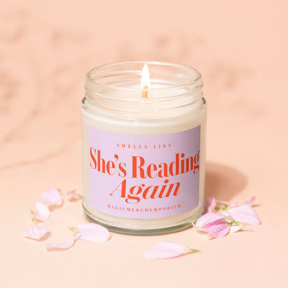 Candle with lit wick, reads "Smells like She's Reading Again. Magicmerch.emporium".
