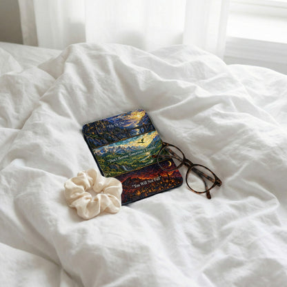 A Kindle case featuring stained-glass fantasy artwork rests on a white comforter beside glasses and a scrunchie.