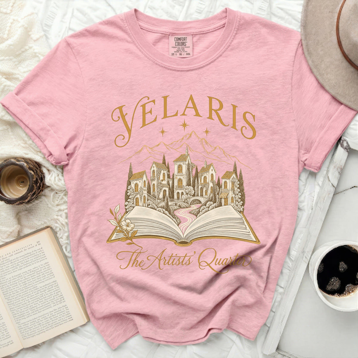 Pink t-shirt with "VELARIS The Artists' Quarter" text and an open book illustration.