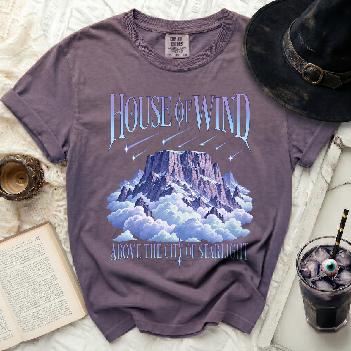 Purple t-shirt with "House of Wind Above the City of Starlight" text and mountain graphic.