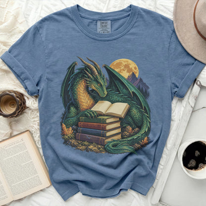Green dragon reading a book on a stack of books with a full moon behind it.