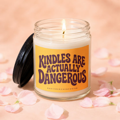Candle with "Kindles are Actually Dangerous" text on orange label, lit flame, black lid.