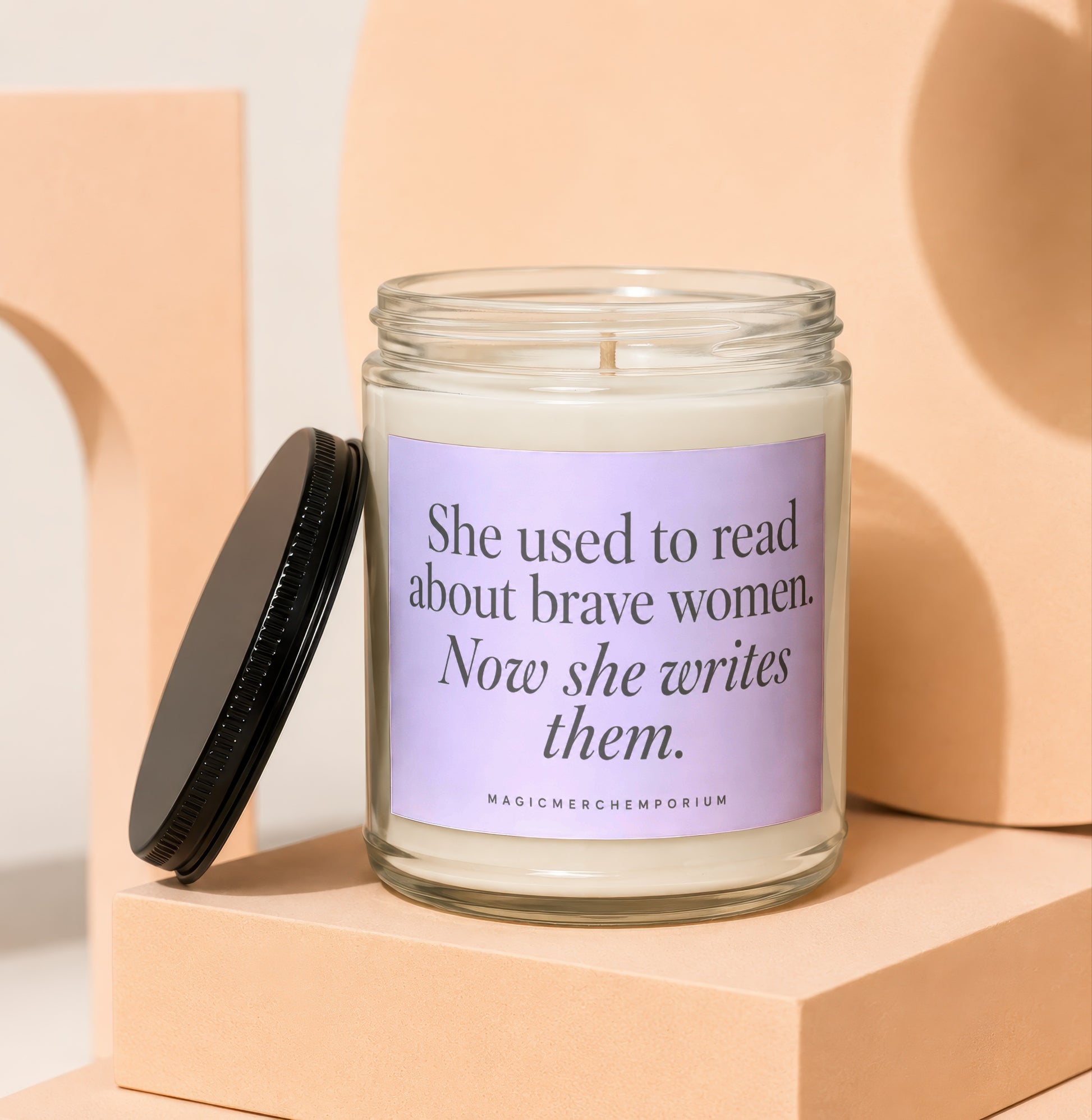 Scented candle with purple label that reads "She used to read about brave women. Now she writes them."