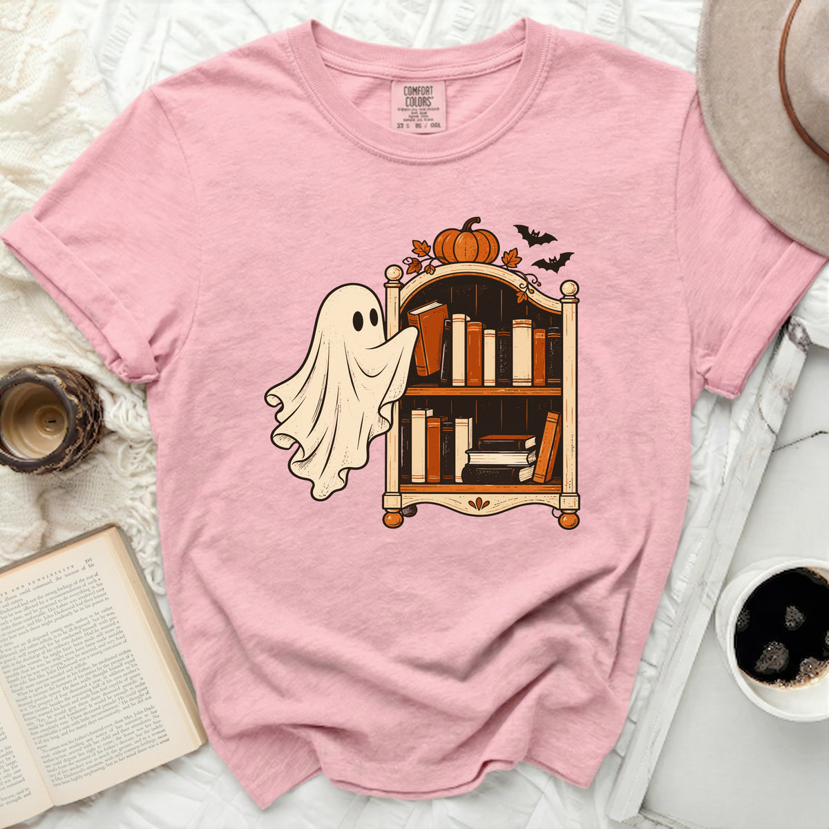 Pink t-shirt with a ghost reaching for books on a shelf with pumpkin and bats.