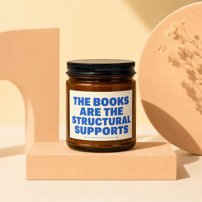 Amber glass candle with blue text "THE BOOKS ARE THE STRUCTURAL SUPPORTS".