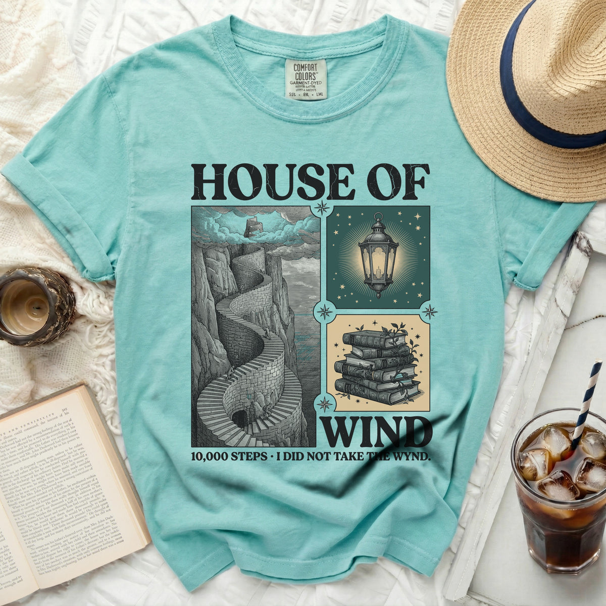 Teal shirt featuring "House of Wind" with illustrations of stairs, lantern, and books.