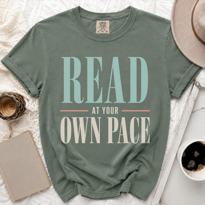 Green t-shirt with "READ AT YOUR OWN PACE" text in large, stylized letters.