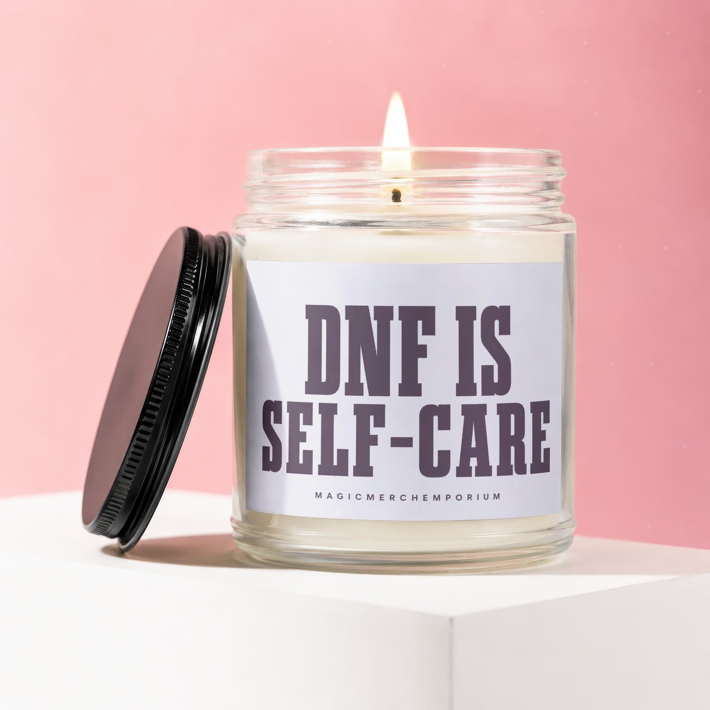 Glass jar candle with lit wick and black lid, reads "DNF IS SELF-CARE".