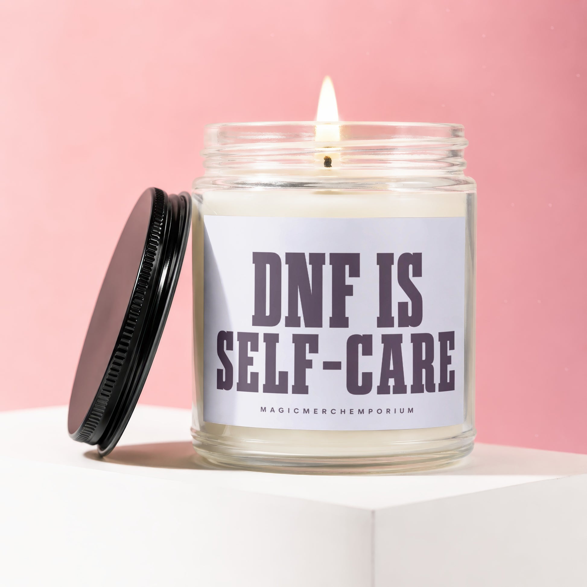 Glass jar candle with lit wick and black lid, reads "DNF IS SELF-CARE".
