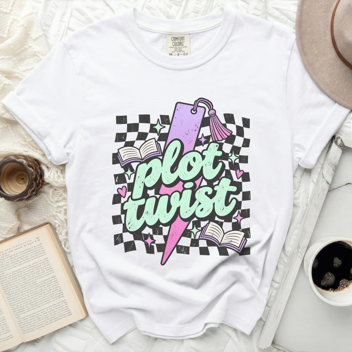 White t-shirt with "plot twist" graphic featuring books, lightning, and checkerboard pattern.
