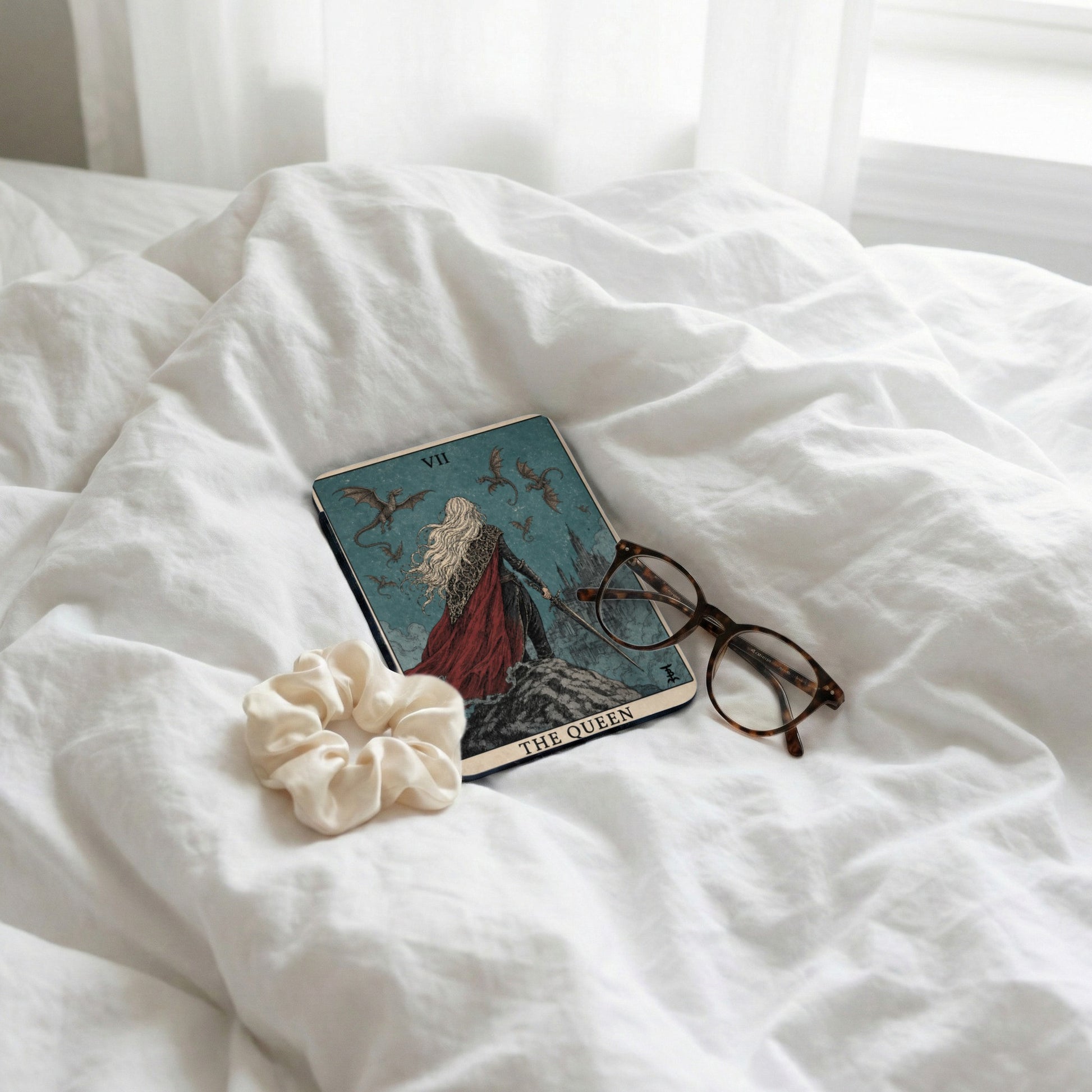 Tarot card, glasses, and scrunchie on white linens.