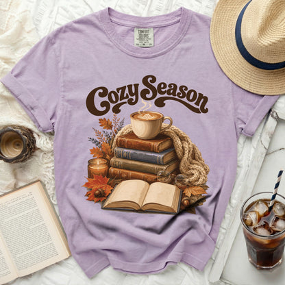 Purple t-shirt with "Cozy Season" graphic featuring books, coffee, and autumn leaves.