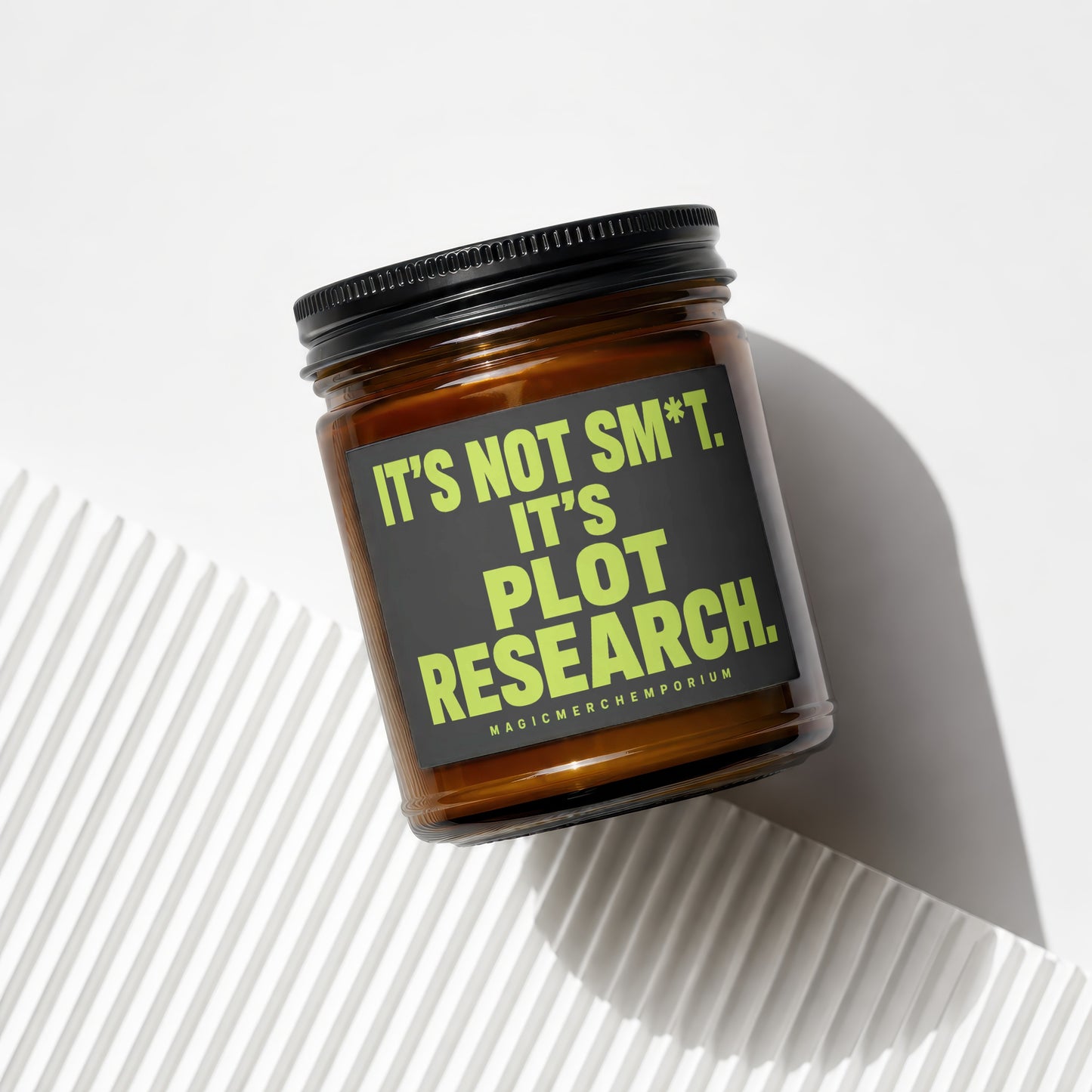 Amber glass candle with black lid and gray label reading "IT'S NOT SM*T. IT'S PLOT RESEARCH."