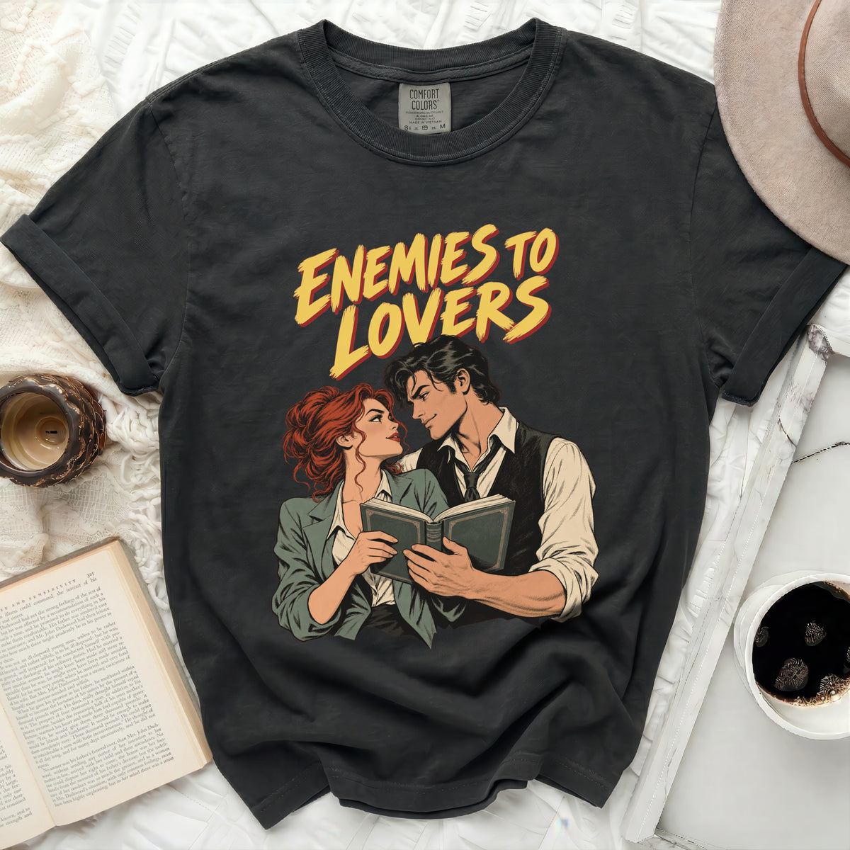 Black t-shirt with "Enemies to Lovers" text and couple reading a book graphic.