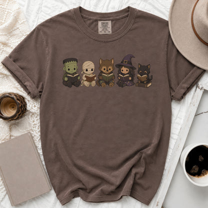 Brown t-shirt with graphic of Frankenstein, mummy, werewolf, witch, and cat reading books.