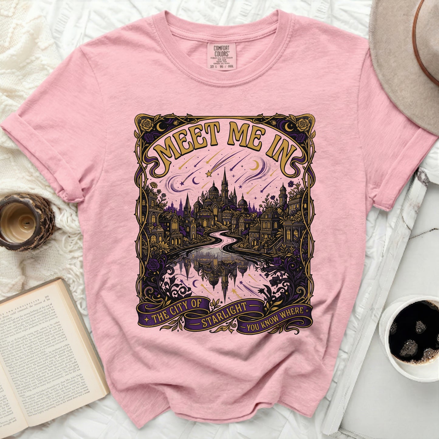 Pink t-shirt with a gold, purple, and pink graphic of a city and stars.