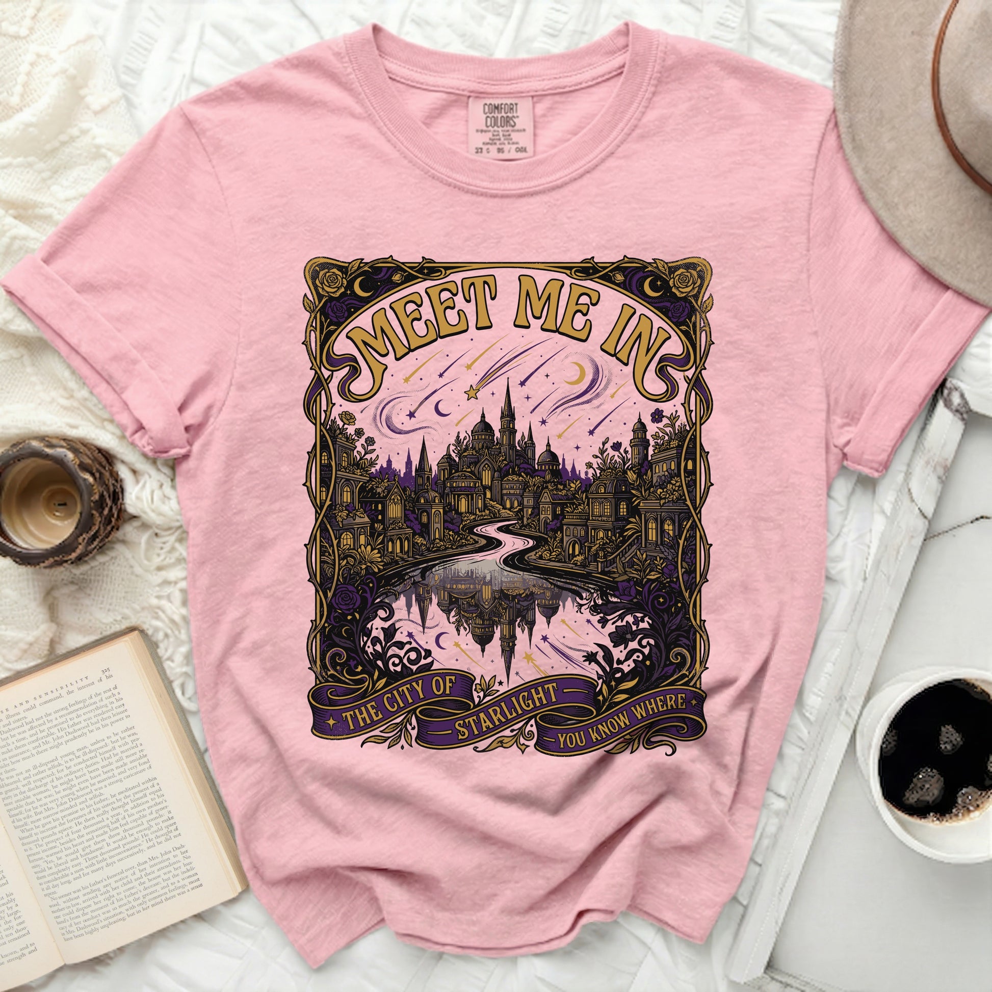 Pink t-shirt with a gold, purple, and pink graphic of a city and stars.