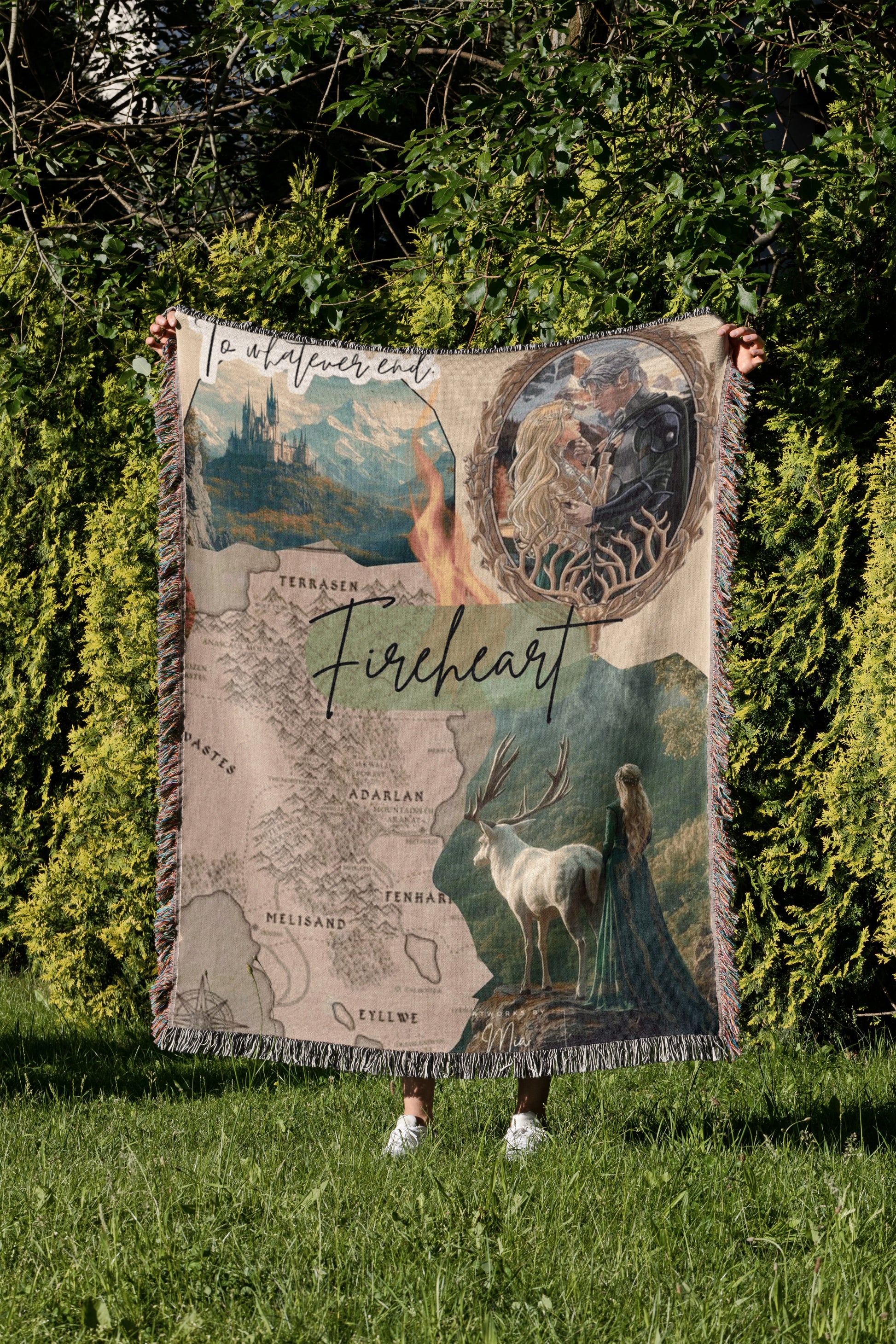 A person is holding a blanket that features a map of the fictional world of "Fireheart" and various scenes from the story, including a castle, a woman with a deer, and a woman in a green dress.