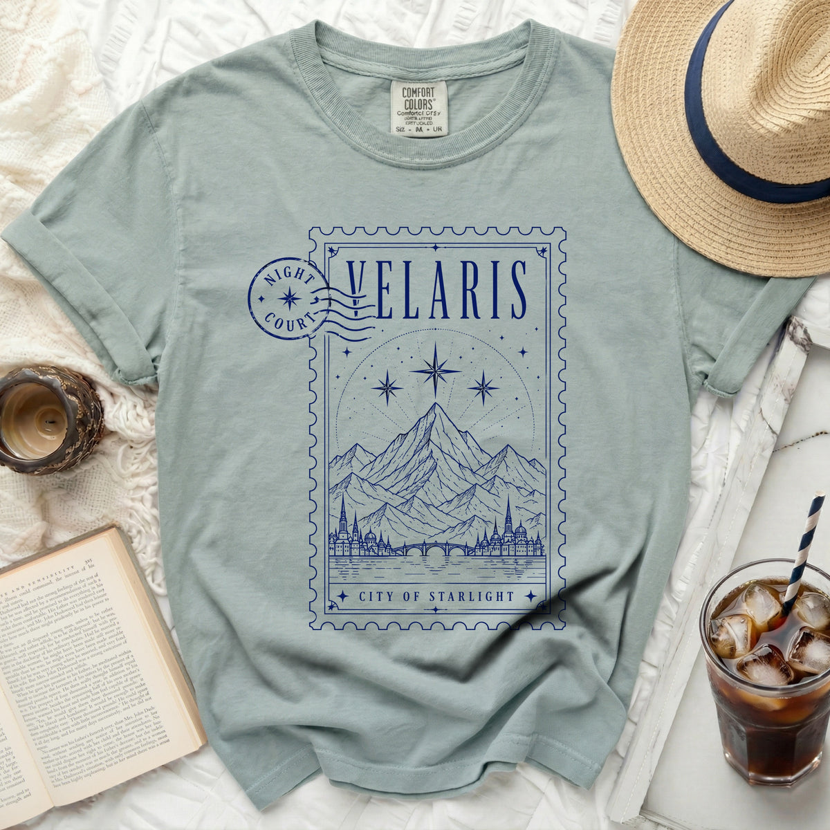 Light blue t-shirt with a blue postage stamp graphic of Velaris, City of Starlight.